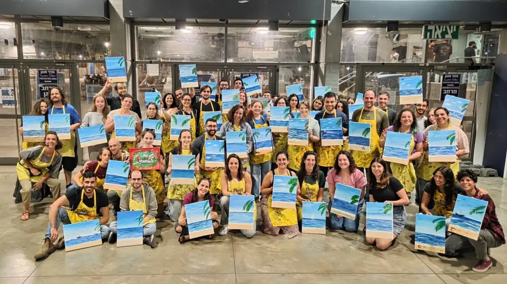 תמונה קבוצתית של המשתתפים עם הציורים שציירו, סדנת ציור PaintPub‏, 2025